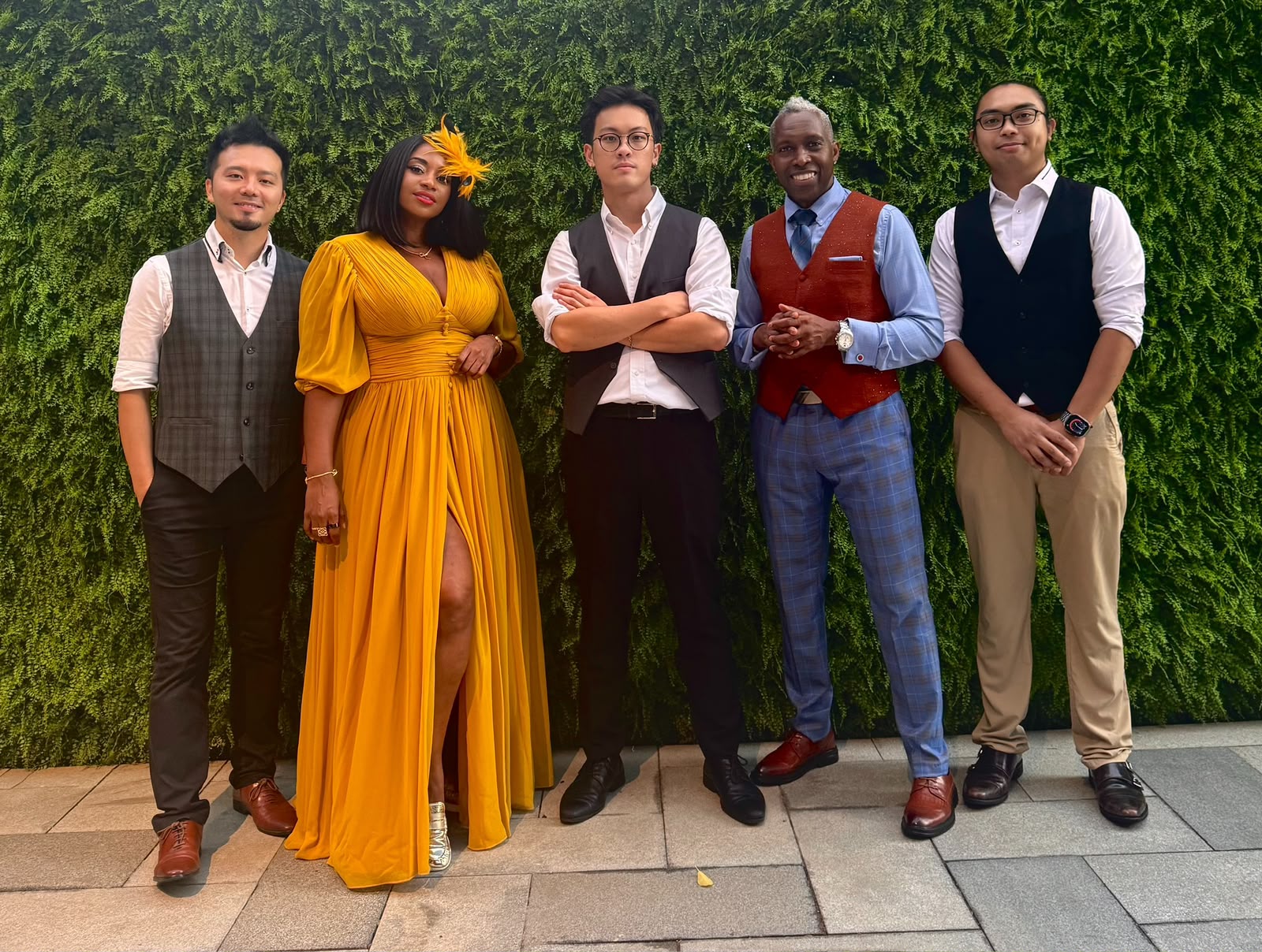 Home 17 The five members of OnPoint in waistcoats and a yellow gown, standing in front of a green plant wall
